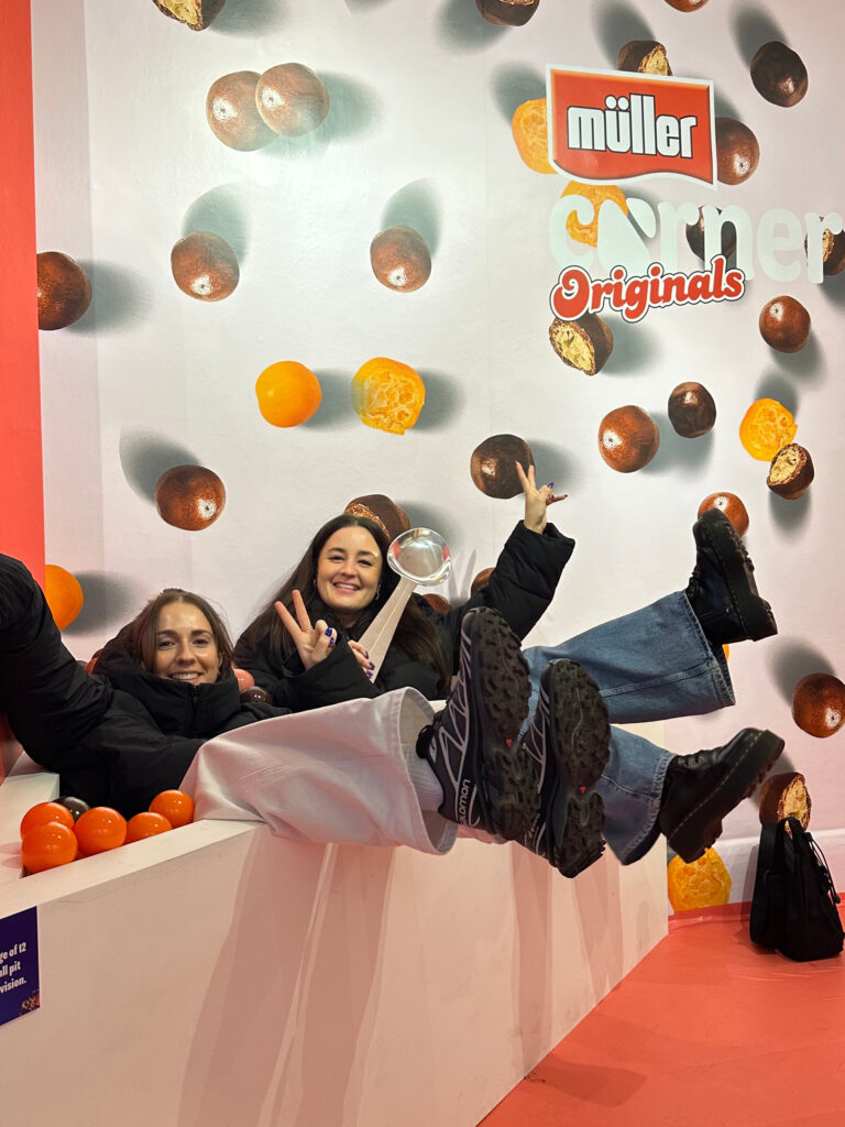 Two people posing playfully in an upside-down room installation with fruit-themed decor.