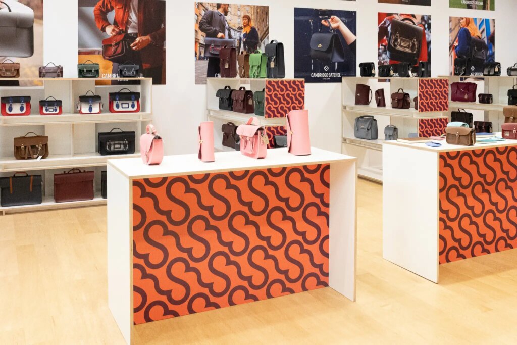 Interior of a fashionable bag store with various satchels on display shelves and promotional images.