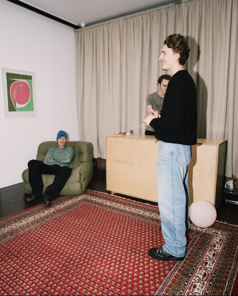 Three people in a cozy living room with patterned rug and minimalist decor.