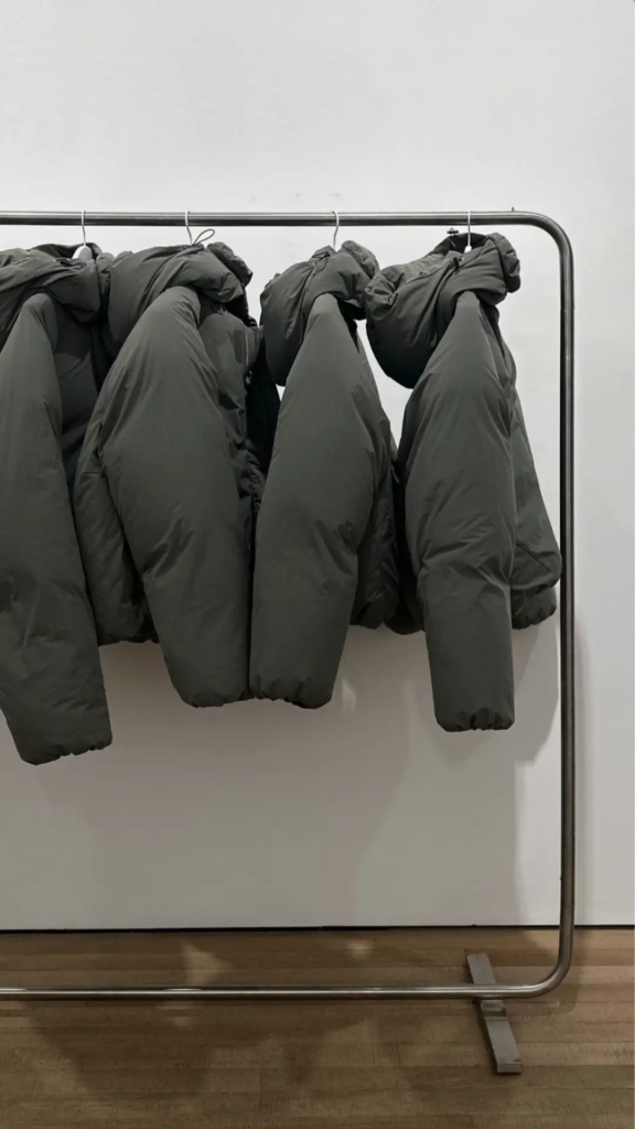Gray winter jackets hanging on a rack against a white wall.