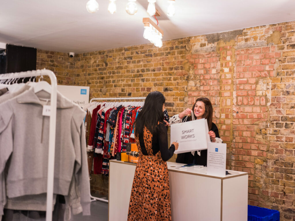 Two women interacting at the checkout counter of a boutique clothing store with exposed brick walls.
