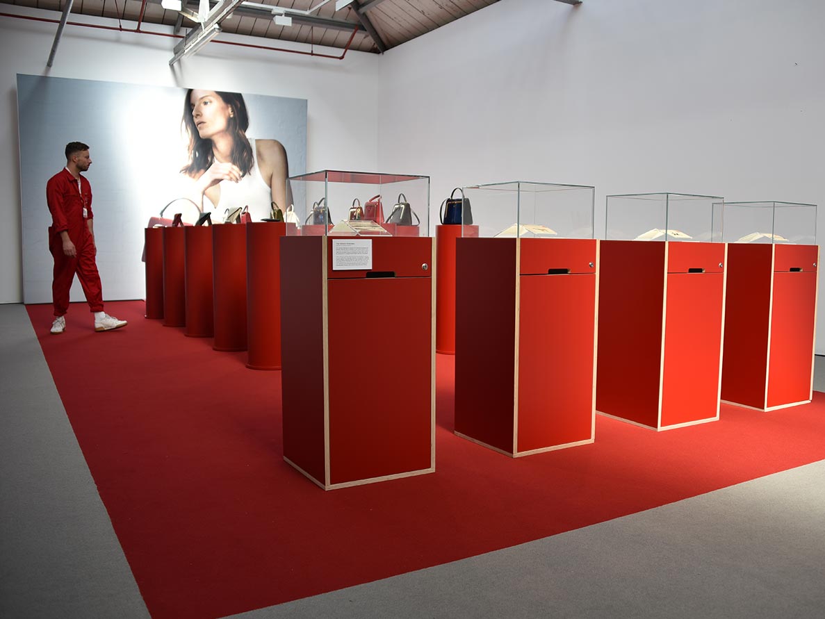 Fashion exhibit with handbags on display and visitor.