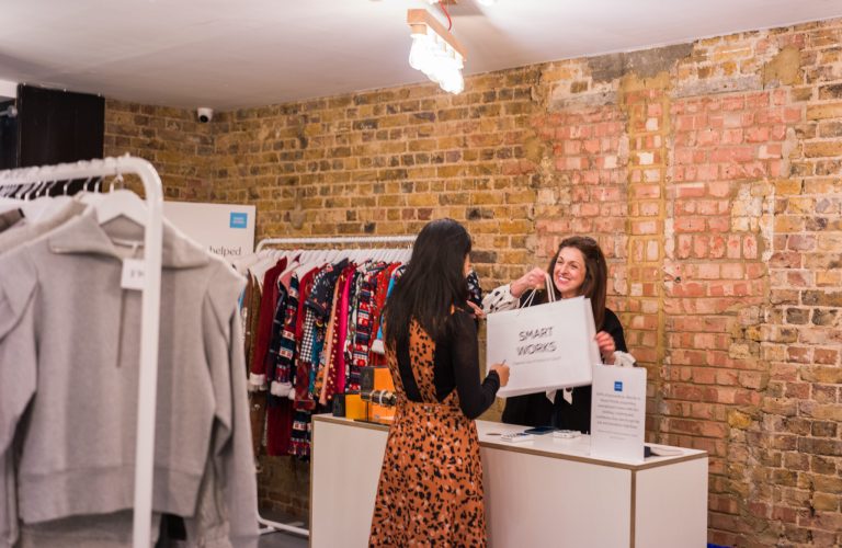 Two women interacting at the checkout counter of a boutique clothing store with exposed brick walls.