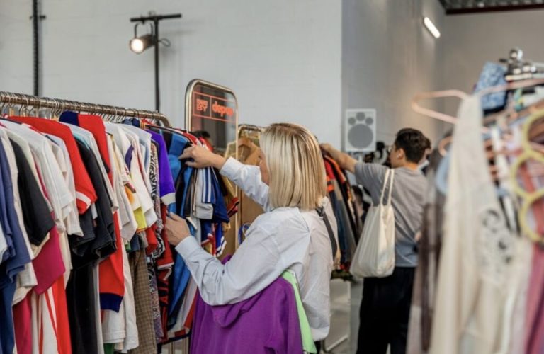 Shoppers browsing through a variety of clothing at a thrift store rack.